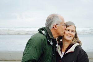 Sterbehilfe ein älterer Mann küssgt eine ältere Frau auf die Wange mit Meer im Hintergrund