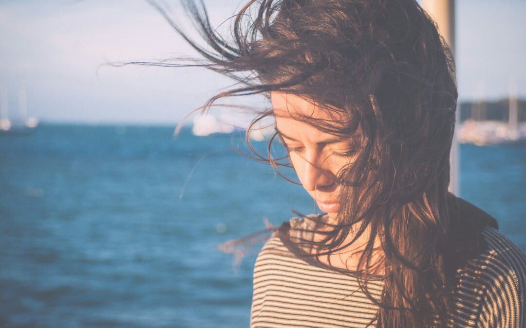 Frau mit wehenden Haaren vor Wasser